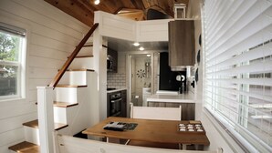 Una cocina compacta con armarios blancos, una escalera de madera y un comedor con mesa de madera.