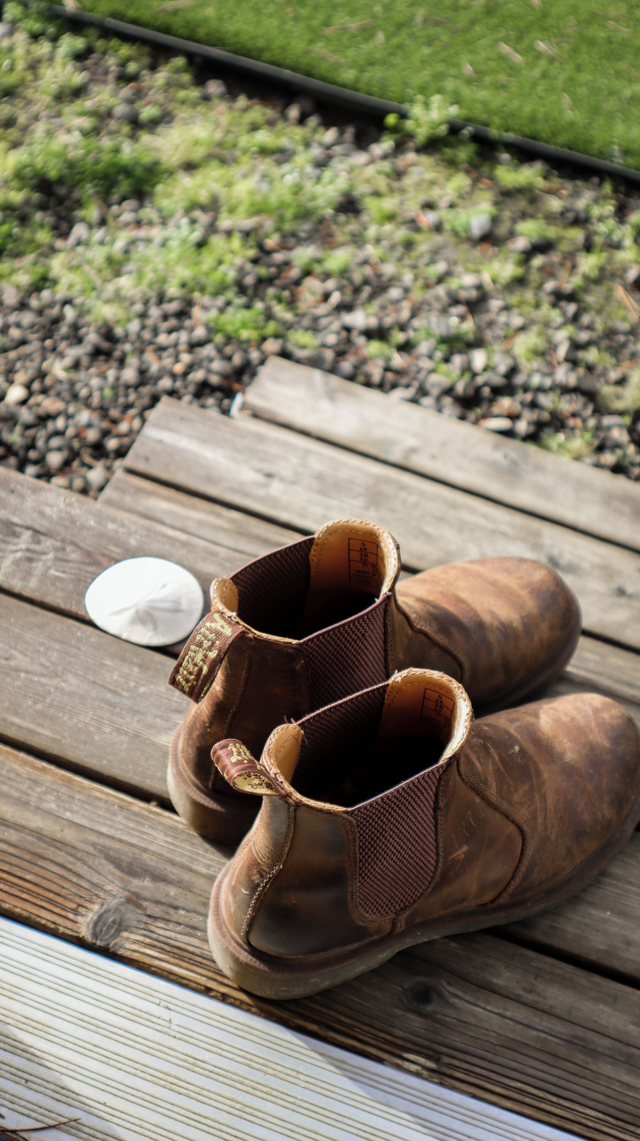 A pair of brown boots on a wooden surface with a small white object nearby.
