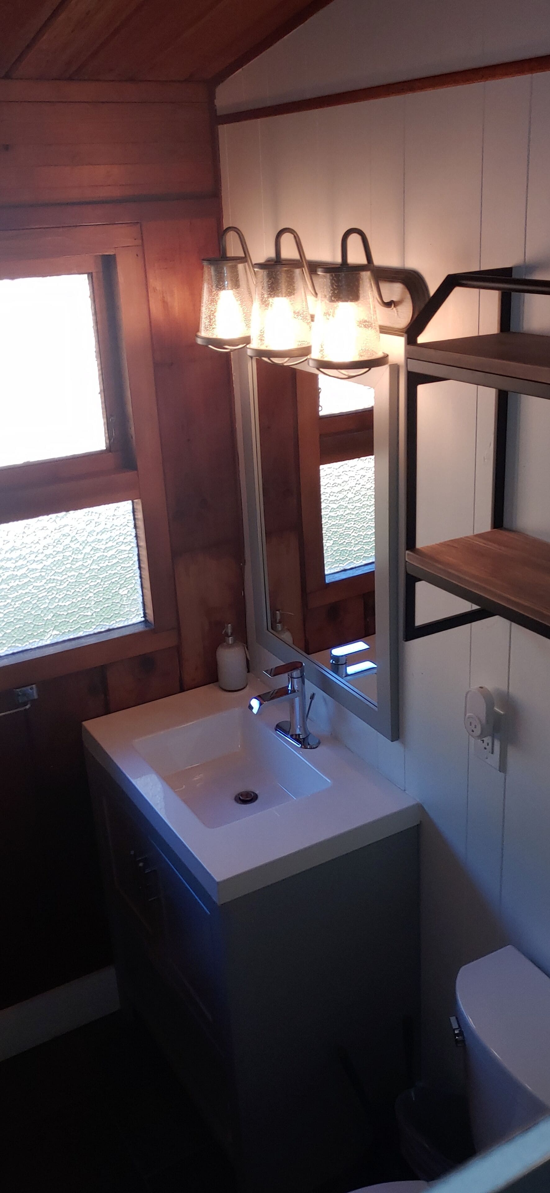 A bathroom with a white sink, a mirror, and a shelf above the sink.