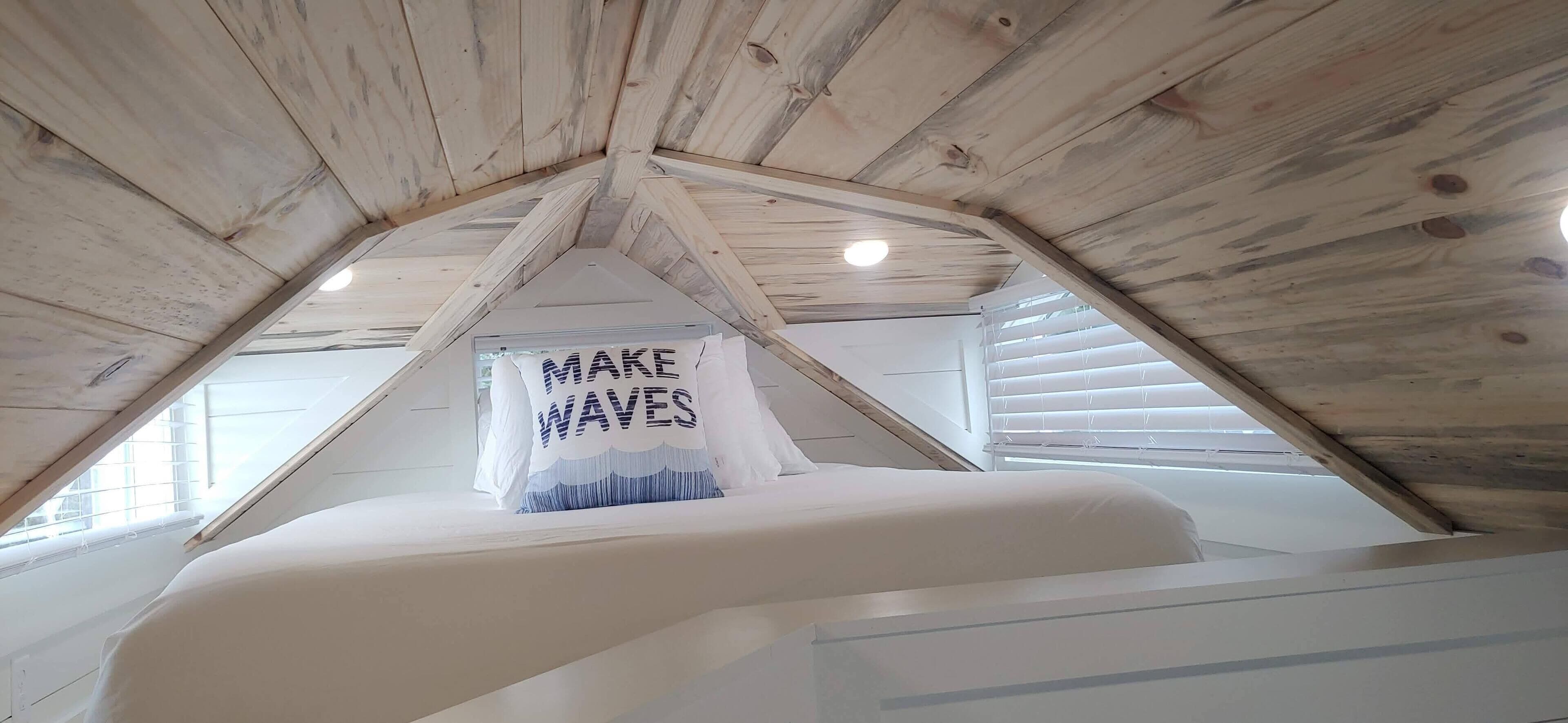 Una habitación con techo inclinado, vigas de madera y una cama con colchón blanco.