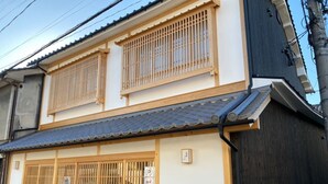 Ein traditionelles japanisches Gebäude mit einem Ziegeldach, Holzschiebetüren und einem kleinen Garten mit Topfpflanzen.