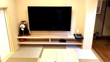 A living room with a flat-screen TV mounted on a wall, a wooden coffee table, and a plush toy on a shelf.