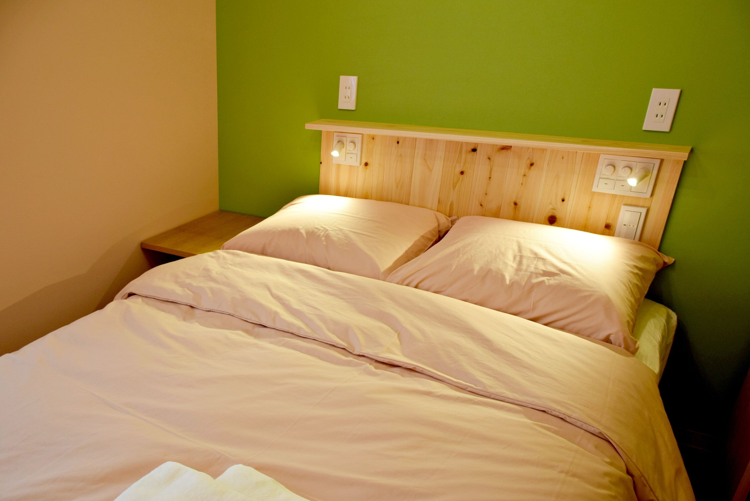 Una cama con cabecera de madera, dos mesitas de noche y una pared verde.