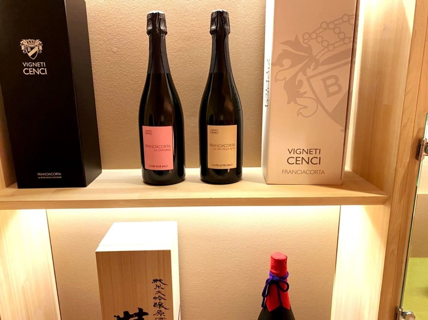 Dos botellas de vino y sus cajas en un estante.