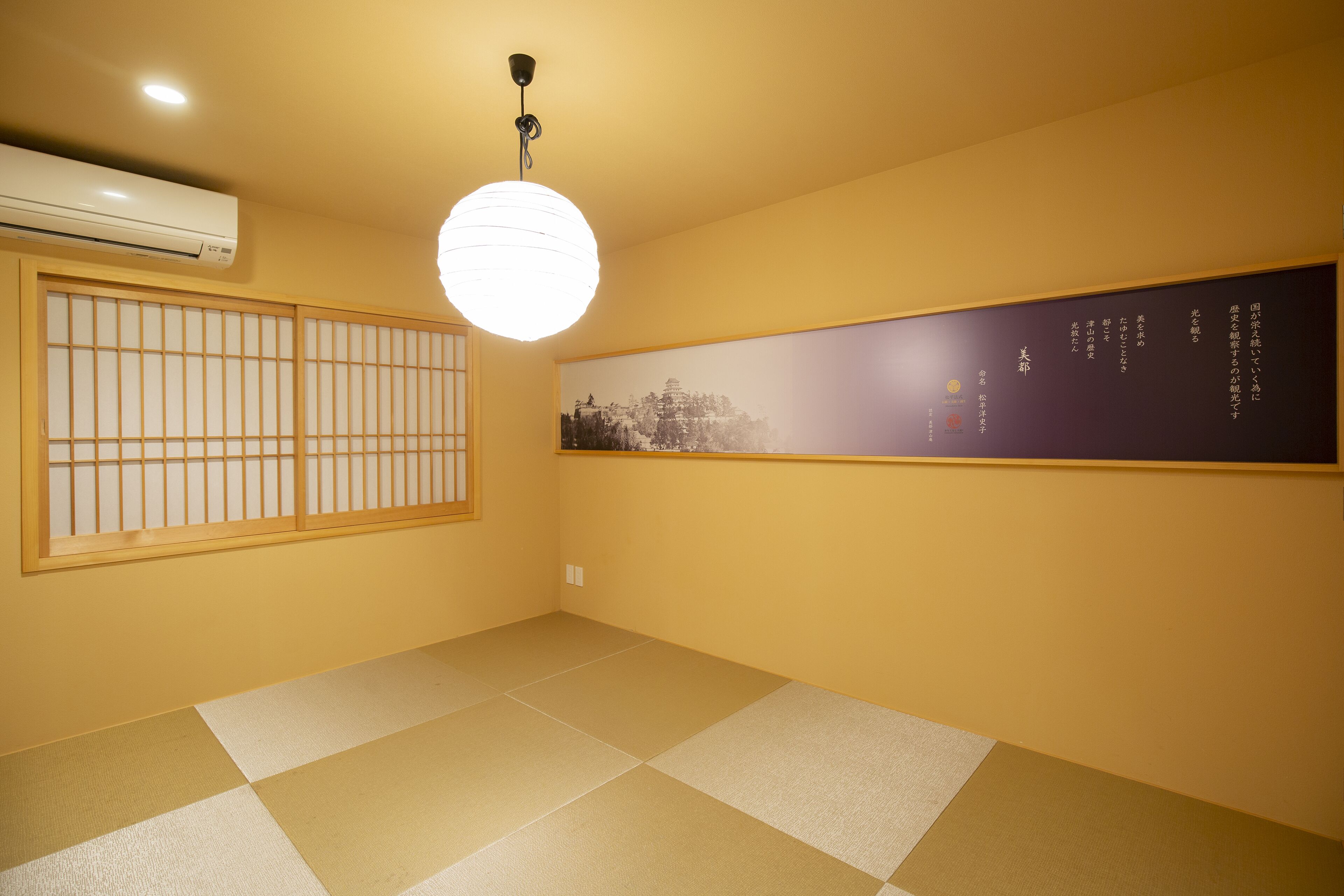 A room with tatami flooring, a shoji screen, a hanging light fixture, and a wall-mounted air conditioner.