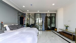 A modern hotel room with a large bed, a desk, and a bathroom visible through a glass door. - Aura Apartment Da Lat (Xuan Huong - Da Lat)
