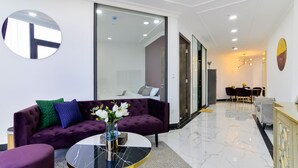 A modern living room with a purple sofa, a round coffee table, and a large mirror. - Aura Apartment Da Lat (Xuan Huong - Da Lat)