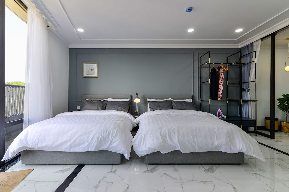 Une chambre moderne avec deux lits, une table de chevet, une lampe, une bibliothèque et une plante en pot.