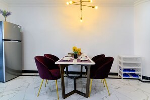 Un comedor con una mesa dispuesta para cuatro, dos sillas, un jarrón con flores amarillas y un estante blanco con objetos azules.