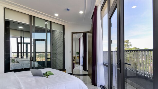 A modern hotel room with a large bed, a laptop, and a balcony with a view. - Aura Apartment Da Lat (Xuan Huong - Da Lat)