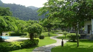 A landscaped garden with a stone pathway leading to a pool, surrounded by lush greenery and hills in the background. - Koh Chang Privilege (Ko Chang)