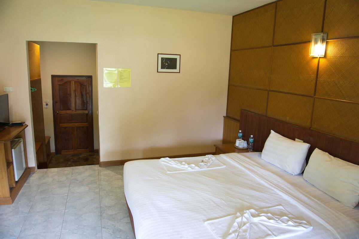 Una habitación de hotel con cama, cabecera de madera, mesita de noche, televisor y puerta.