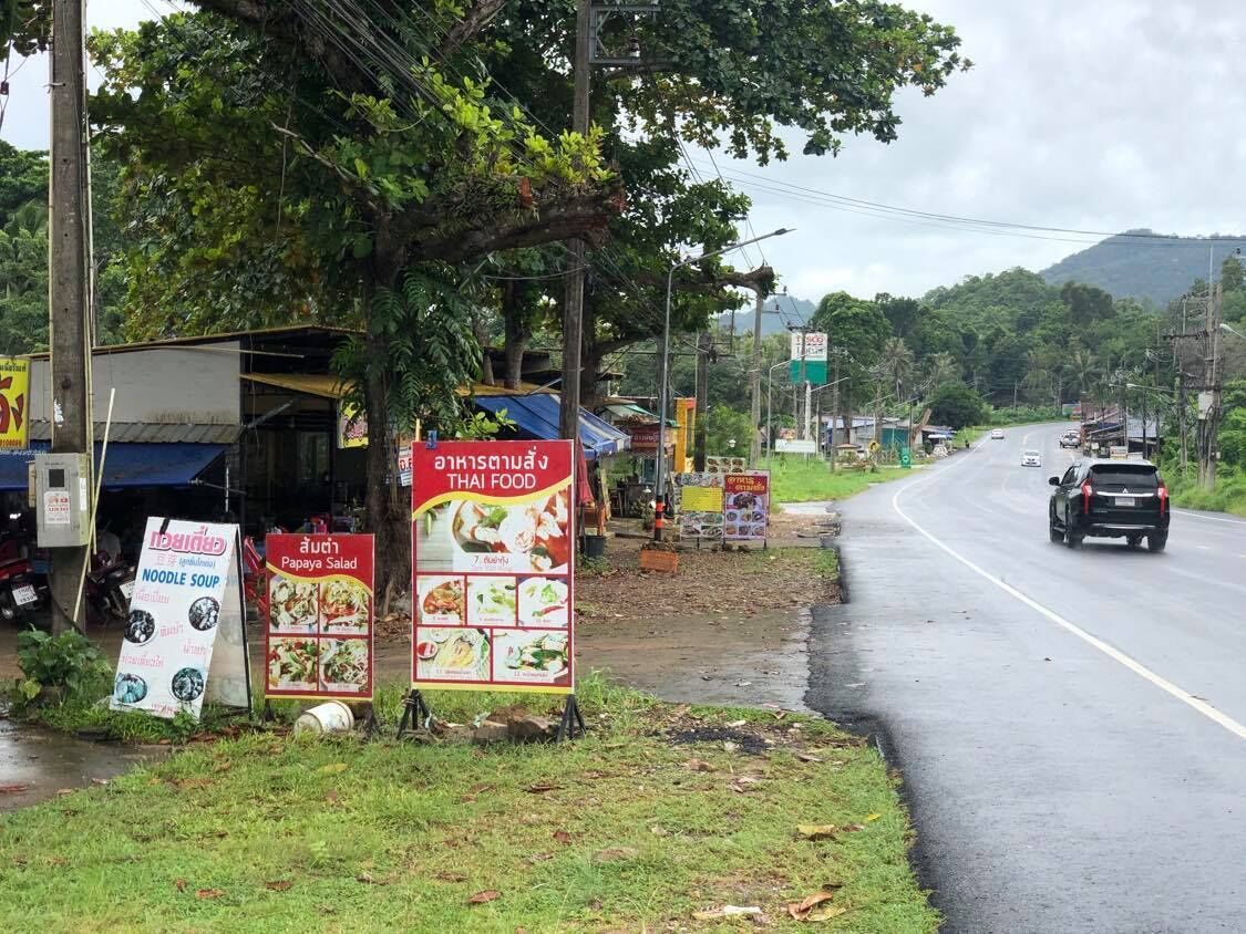 A roadside with food stalls advertising noodle soup and papaya salad.