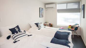 A hotel room with two beds, a window with a view, a colorful chair, and an air conditioning unit.