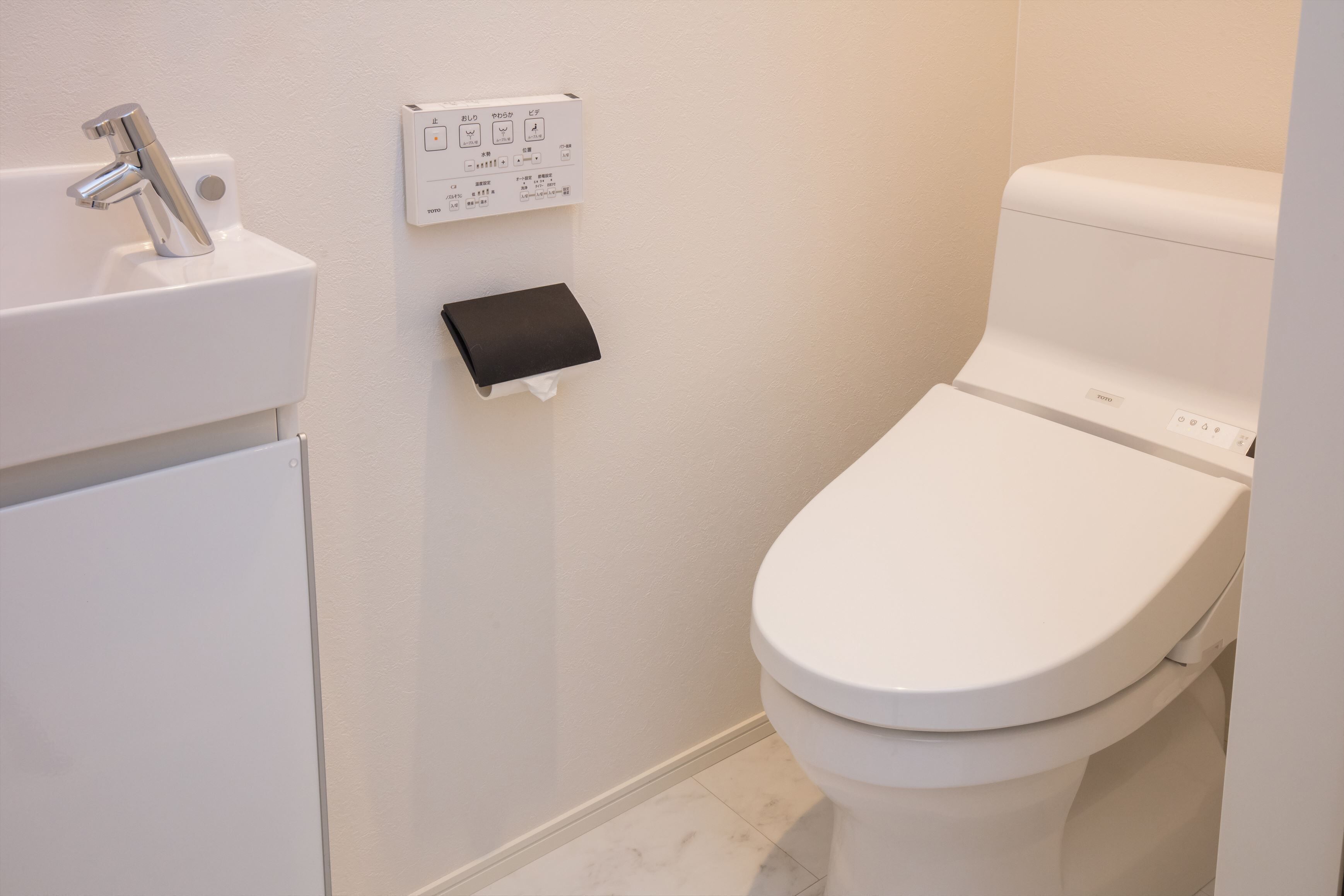 A modern bathroom with a white toilet, a sink with a faucet, and a control panel on the wall.