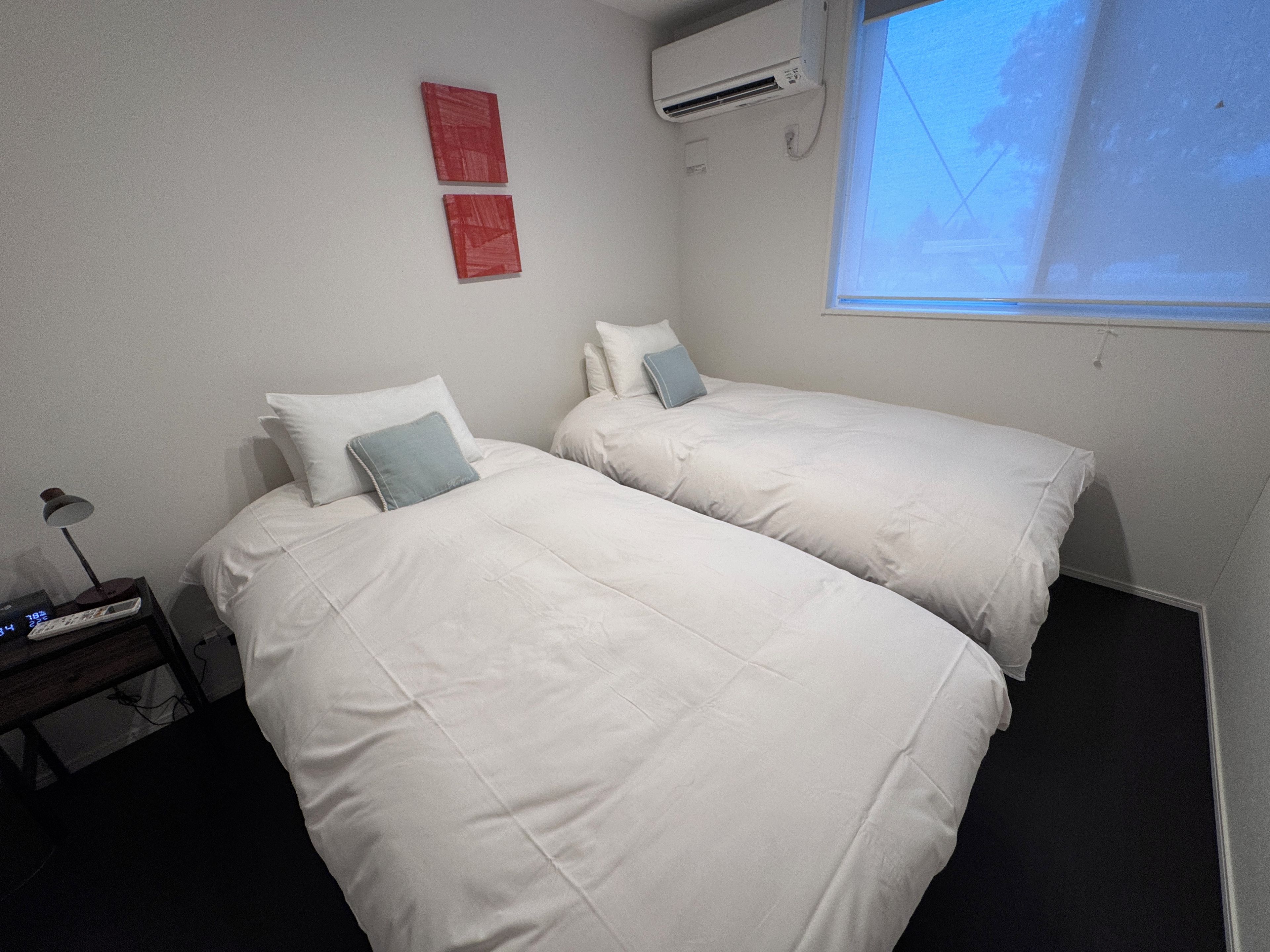 Hotellihuone, jossa on kaksi sänkyä, yöpöytä lampun kanssa ja ikkuna, josta on näkymä.