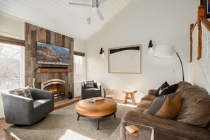 Un salon avec une cheminée, un grand tableau et un ventilateur de plafond.