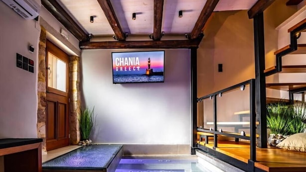Een modern interieur met een stenen muur, een houten deur en een televisie waarop 'CHANIA GREECE' staat.