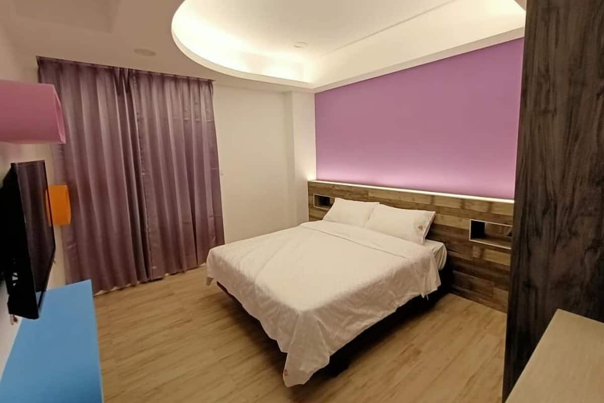 A modern hotel room with a wooden bed, a purple accent wall, and a ceiling light fixture.