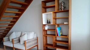 Una scala con ringhiere in legno, un divano bianco imbottito con cuscini e una libreria in legno con numerosi ripiani.