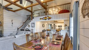 A dining area with a wooden table set for six, surrounded by wooden chairs. A staircase with a railing leads to an upper level.
