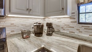 A kitchen with white cabinets, a marble countertop, a Keurig coffee maker, and a glass coffee pot.