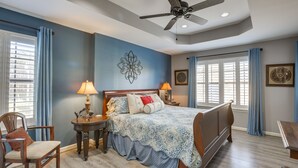 A bedroom with a bed, two bedside tables, a chair, a ceiling fan, and a window with curtains.