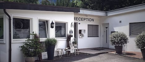 Zona de recepción con un cartel, un espacio de asientos pequeño y plantas en macetas.