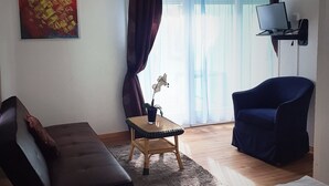 A modern living room with a sofa, a blue armchair, a small table with a plant, and a large window with curtains. - Inter-Alp (Saint-Maurice)