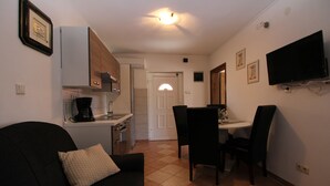 A compact living space with a kitchenette, a dining area with a table and chairs, and a black sofa with a cushion. - Apartment 934/2231 (Istria - Fažana), 500m from the beach (Fažana)