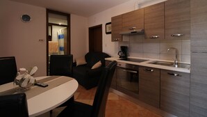 A compact kitchen with a built-in oven, a sink, and wooden cabinets. There is a dining area with a table and chairs. - Apartment 934/2231 (Istria - Fažana), 500m from the beach (Fažana)