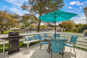 Eine Terrasse mit Grill, Tisch und Stühlen sowie einem großen Sonnenschirm.