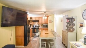 A compact kitchen with wooden cabinets, a dining table, and a TV mounted on the wall.