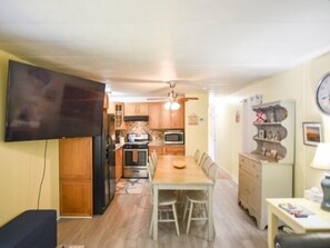 Una cocina compacta con armarios de madera, una mesa de comedor y un televisor montado en la pared.