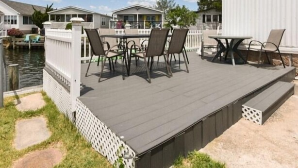 A deck with outdoor furniture, a white fence, and a body of water in the background.