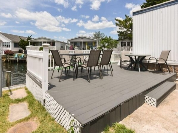 Una terraza con mobiliario exterior, una valla blanca y una masa de agua al fondo.