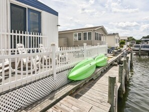 Um cais com cerca branca, uma fileira de barcos verdes e uma fileira de casas à beira-mar.