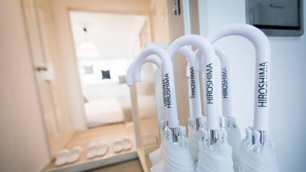 A row of white umbrellas with the brand name "HIROSHIMA" on them, hanging on a wall in a hotel corridor. - Dai3Himawari  401 (Hiroshima)