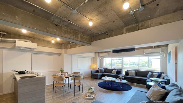 A modern kitchen with a dining area, a sofa set, and a large window providing natural light.