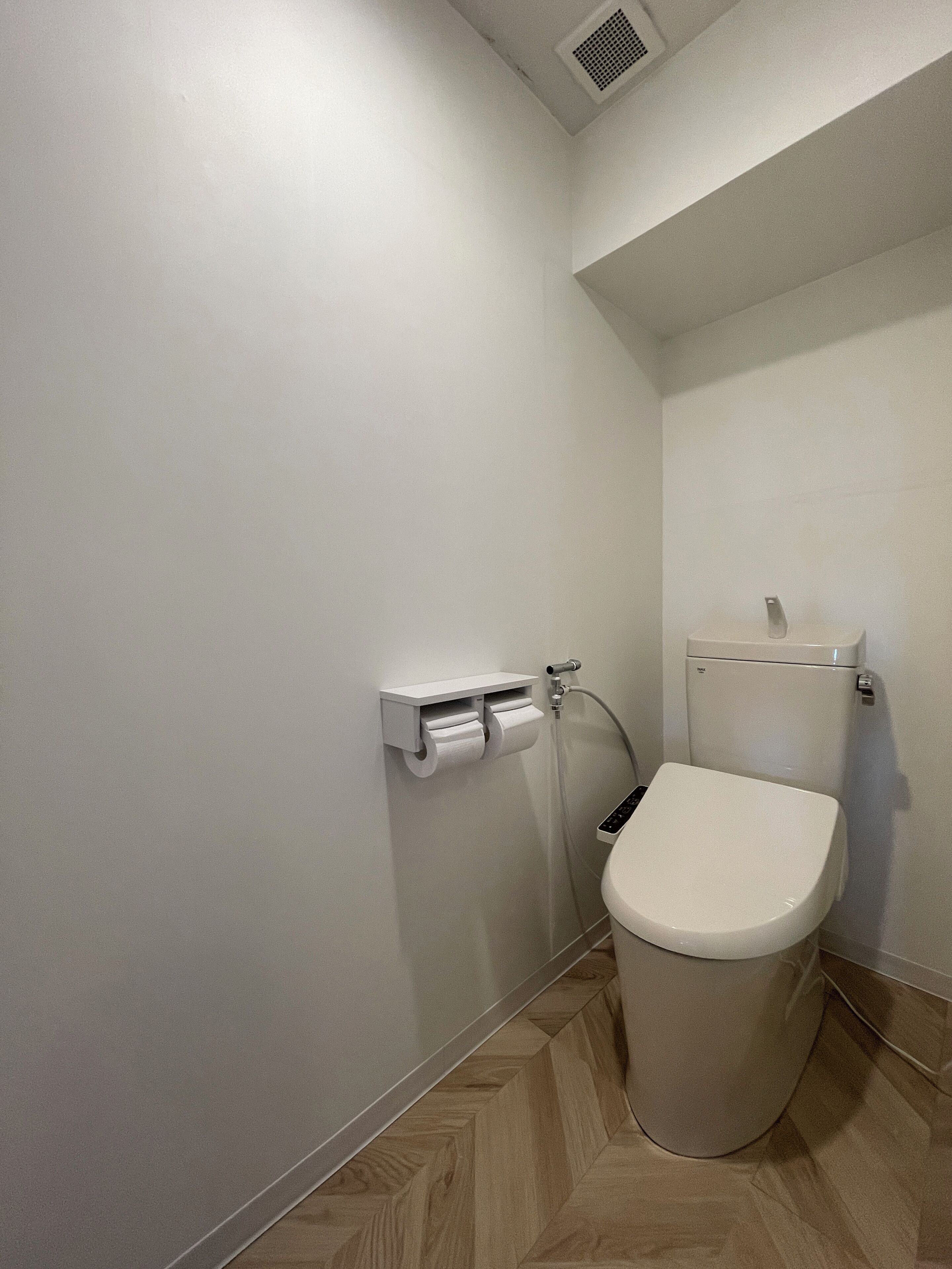 Ein kleines, modernes Badezimmer mit Toilette, Papierhandtuchspender und Duschkopf.