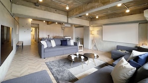 A spacious living area with a large grey sofa, a smaller grey sofa, and a coffee table. There is a dining area in the background with a table and chairs. -  Dai3Himawari 604 (Hiroshima)