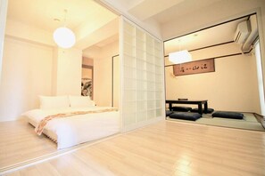 Un dormitorio con cama, puerta de cristal corredera y una pequeña mesa con cojines.
