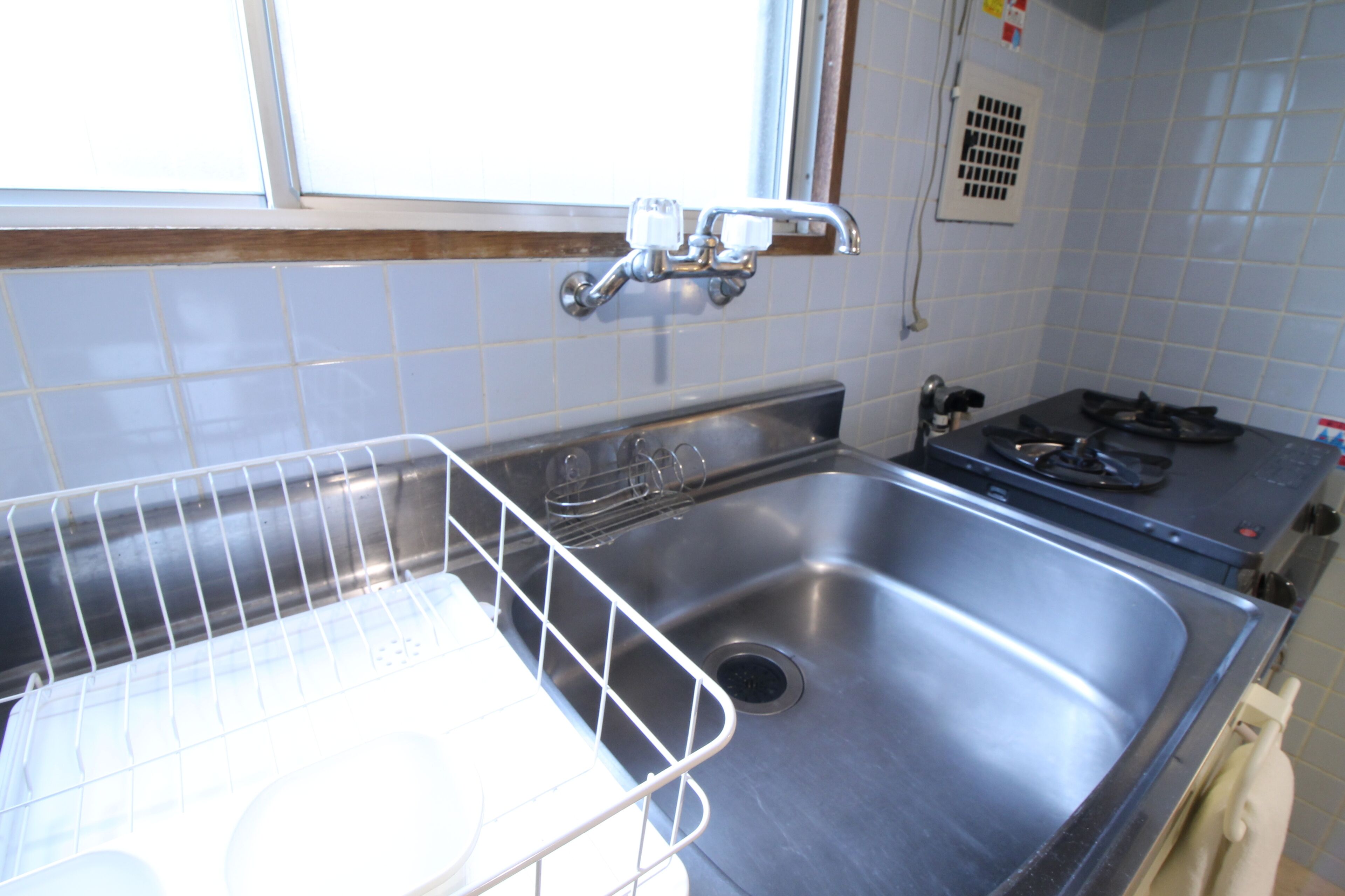 A stainless steel kitchen sink with a dish rack, a window above the sink, and a tiled backsplash.