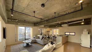 A spacious living area with a large sofa, a dining table, and a kitchen area. - M's Lea Building (Hiroshima)