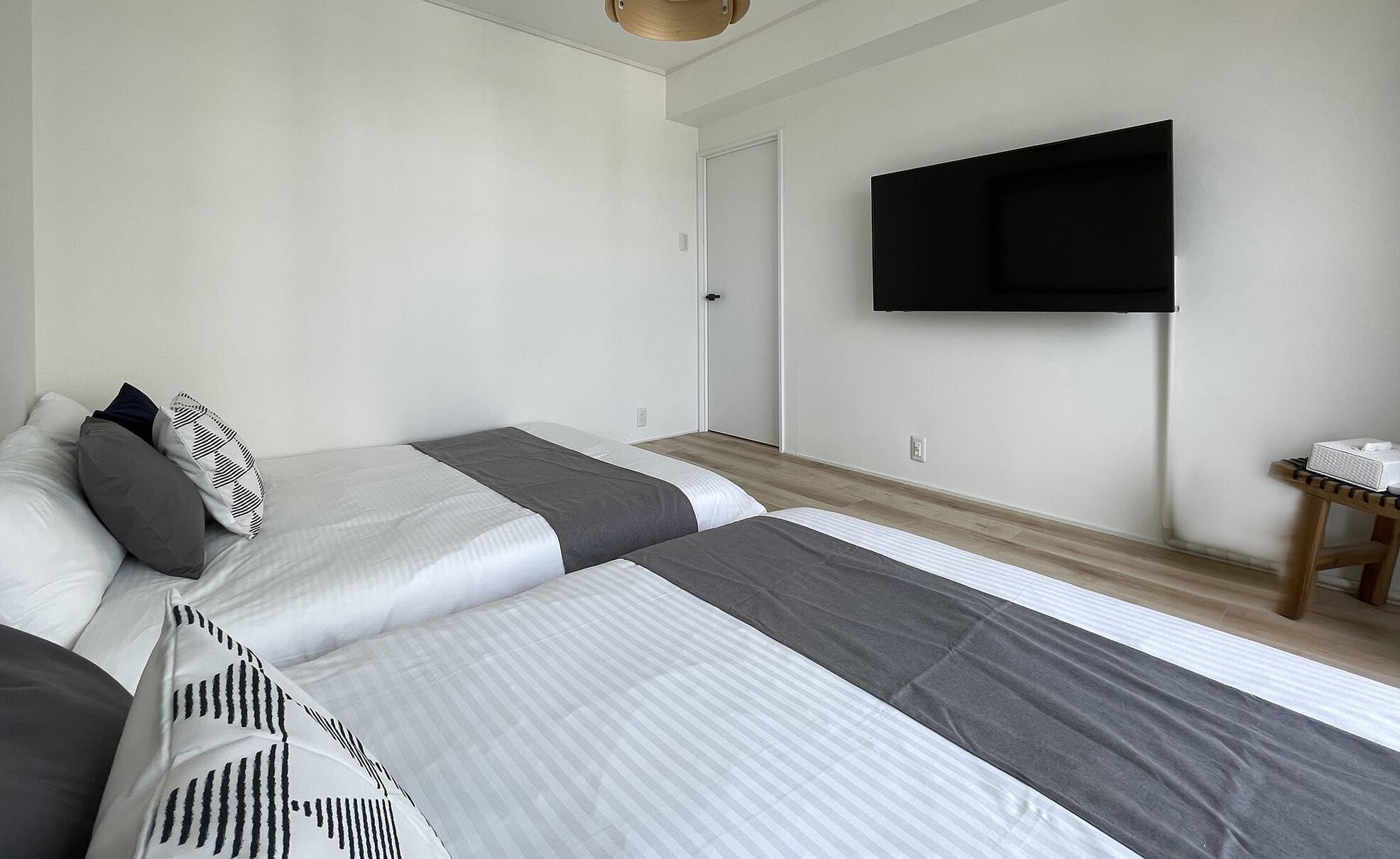 Una habitación de hotel moderna con dos camas, un televisor de pantalla plana montado en la pared y una mesita de noche de madera.