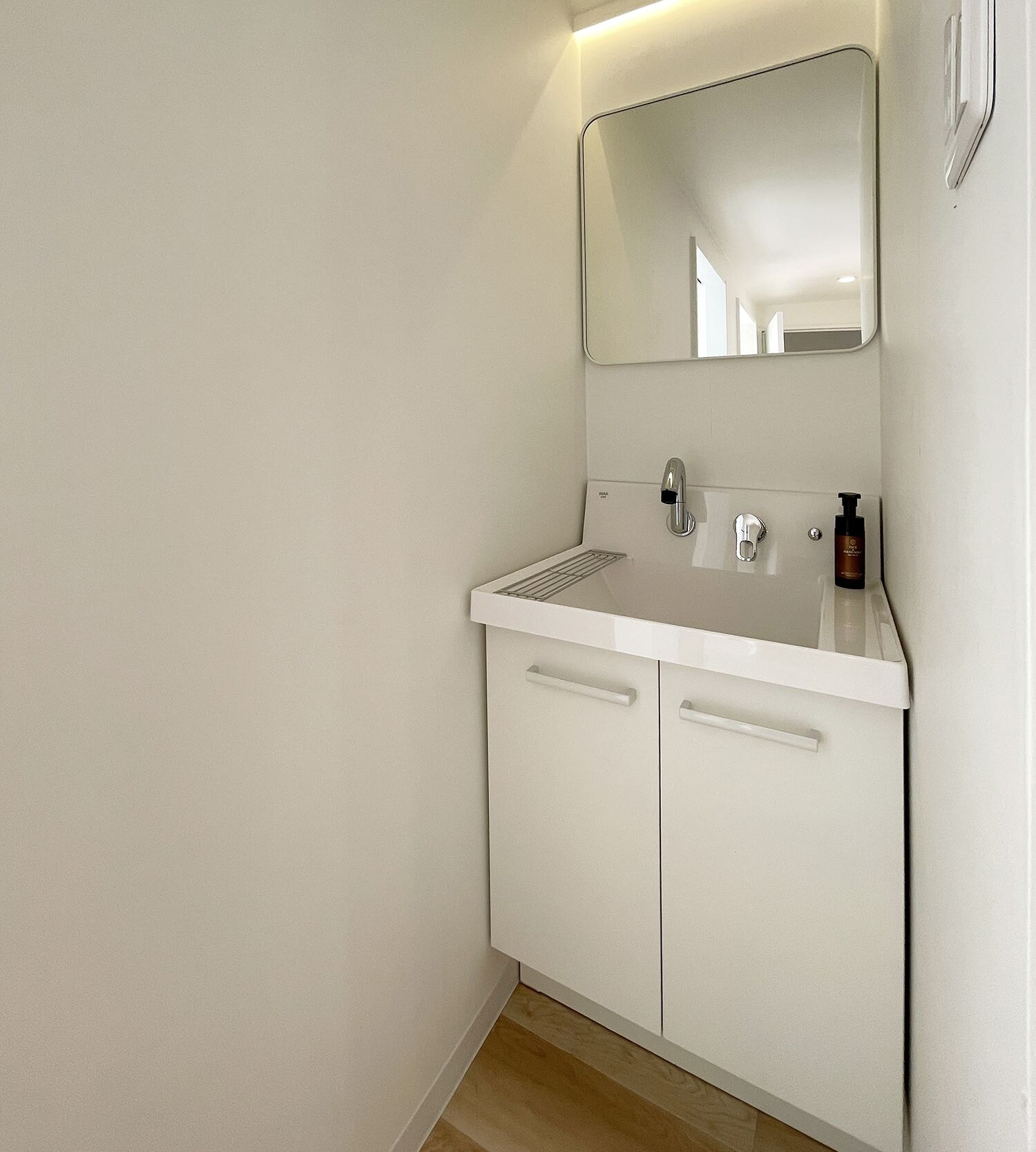 Une petite salle de bain blanche, avec un seul lavabo, un miroir et deux armoires.