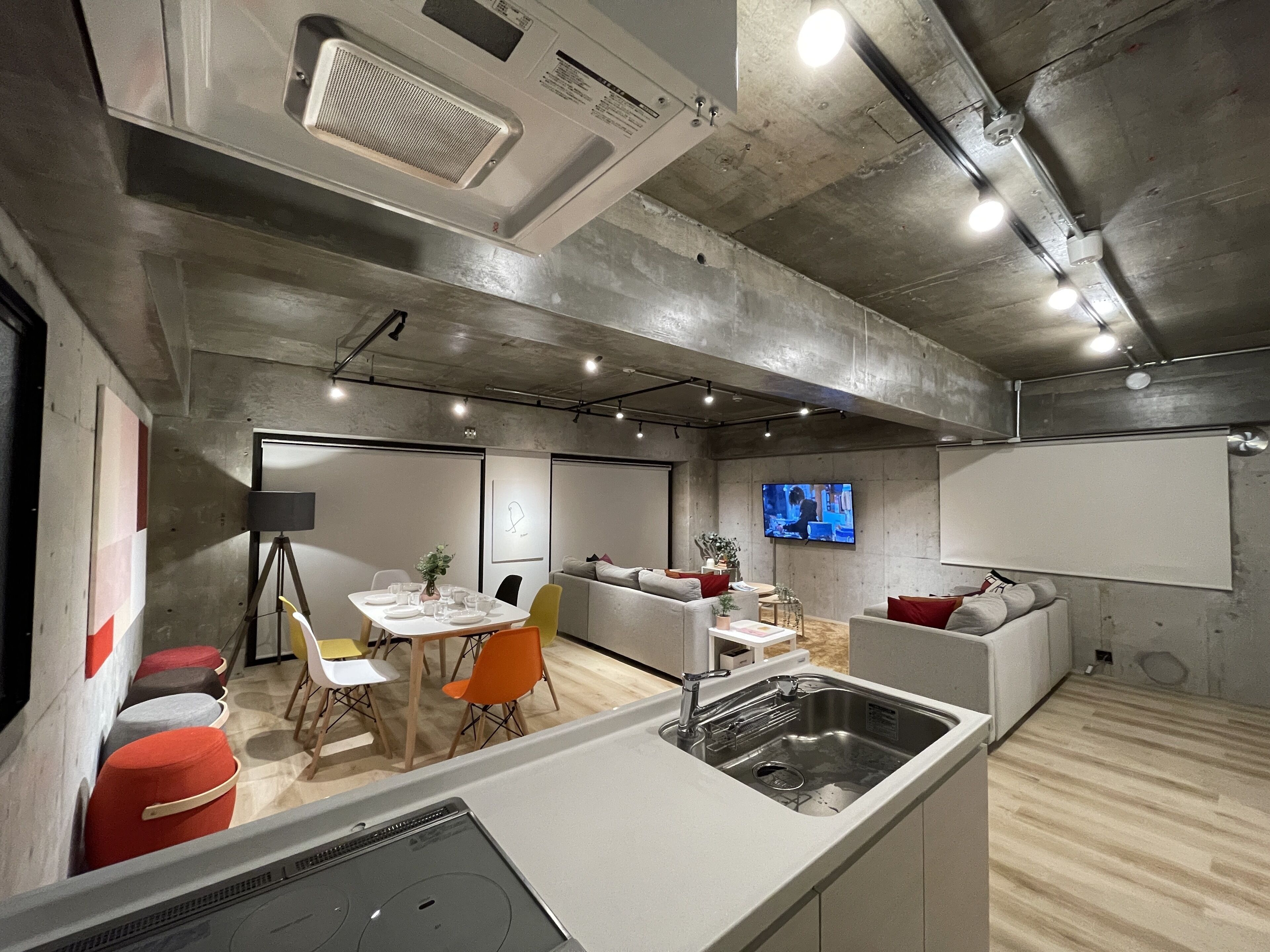 Cozinha moderna com pia embutida, área de refeições com mesa e cadeiras, e sala de estar com sofá e TV na parede.