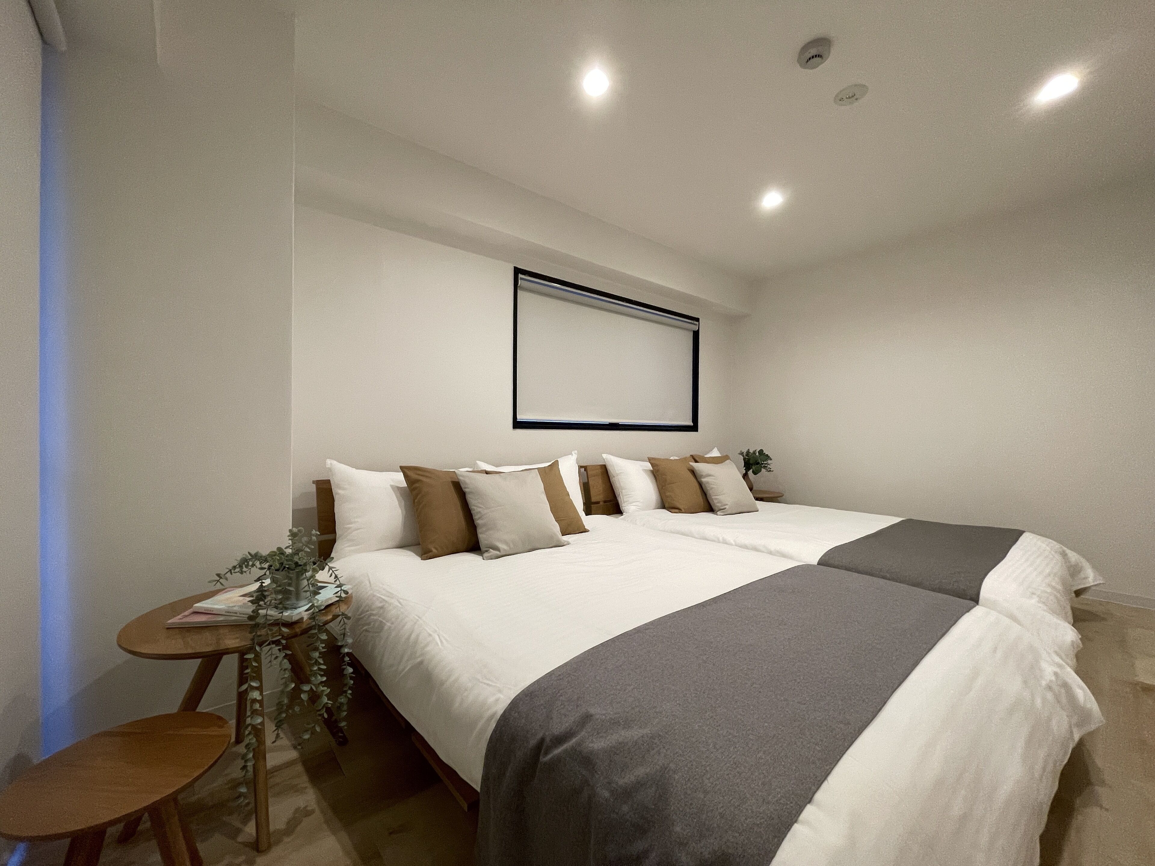 A neatly arranged hotel room with a large bed, a small table with a plant, and a wall-mounted projector.