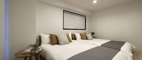 A neatly arranged hotel room with a large bed, a small table with a plant, and a wall-mounted projector.