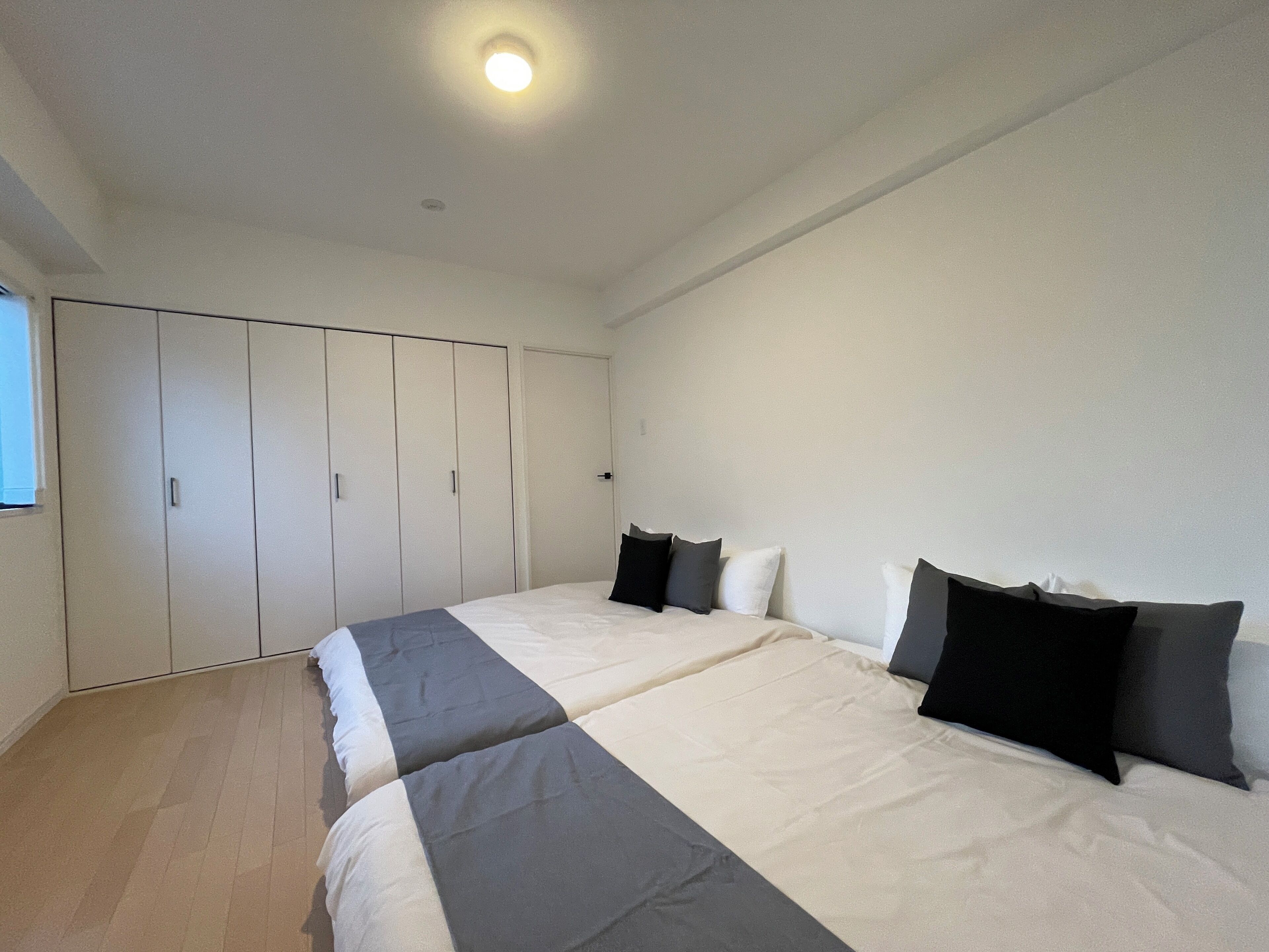 A bedroom with two beds, a wardrobe, and a ceiling light.